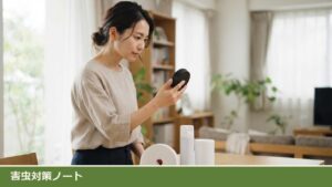 明るいリビングのテーブルの前で、女性が黒くて丸い平たい容器を手に取って見ている。テーブルには白い隙間テープのロールと白いスプレー缶、白い円筒形の容器が並んでいる様子