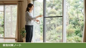 リビングの掃き出し窓の前で、女性が白い無地の隙間テープのロールを持ち、網戸の枠の縁に当てる位置を指で確かめている様子